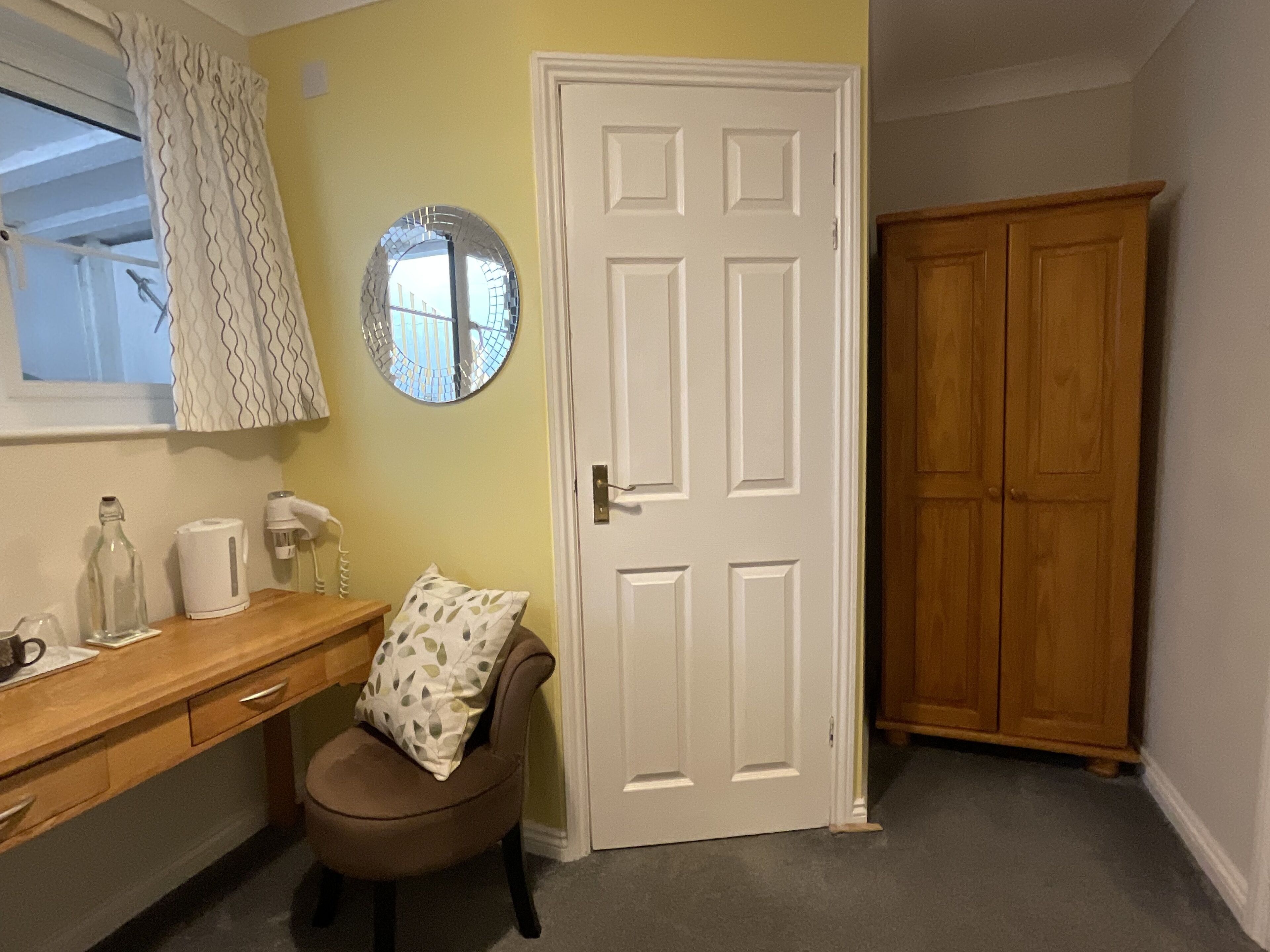 A room with a wooden desk, a chair, a white door, and a wooden wardrobe.
