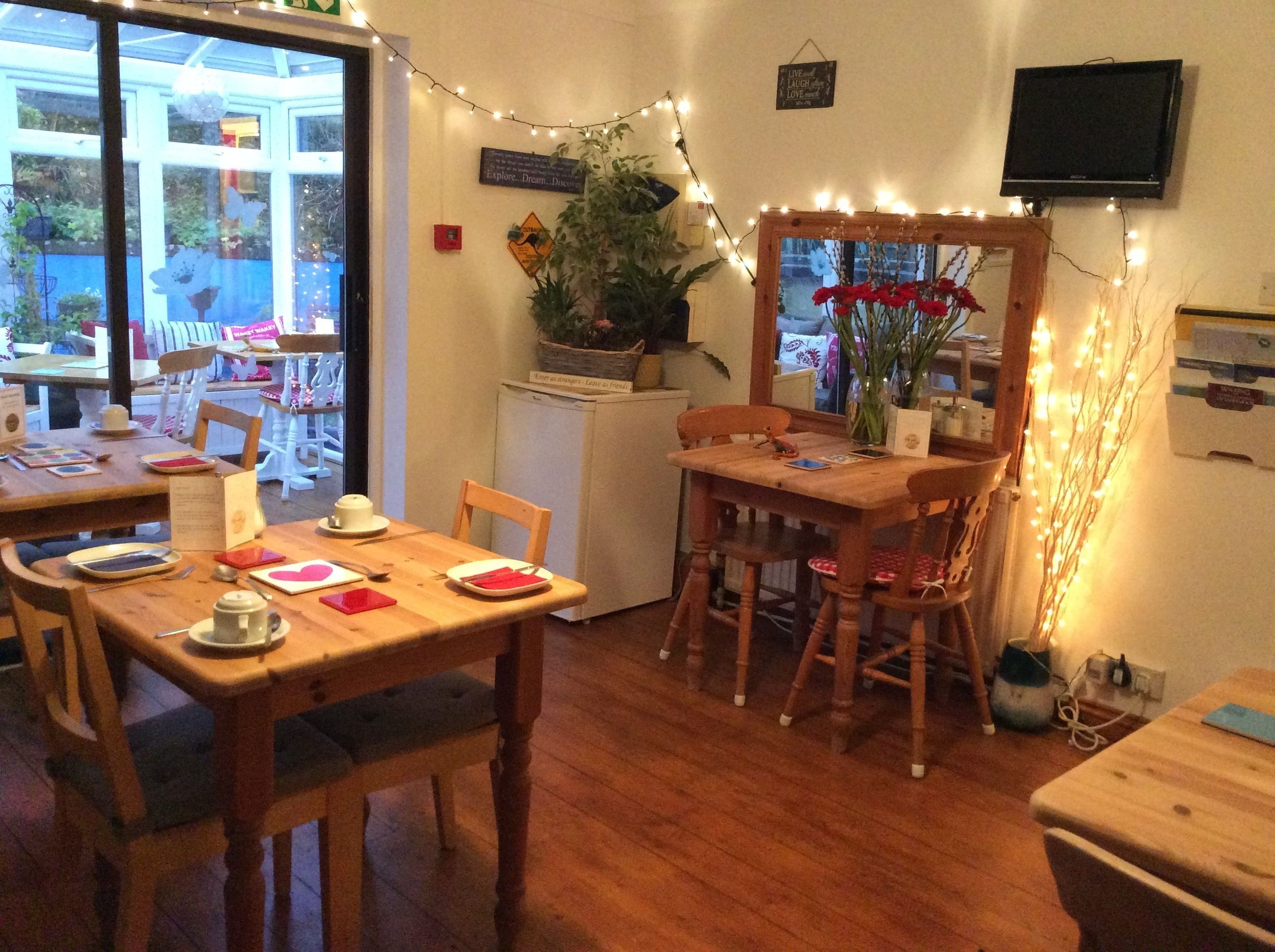 A cozy dining area with wooden tables and chairs, string lights, and a television mounted on the wall.