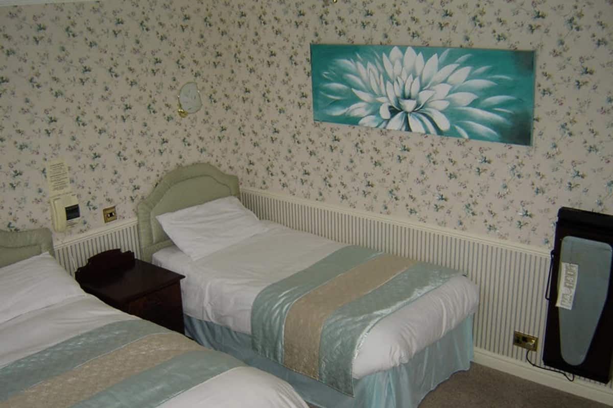 A bedroom with two beds, floral wallpaper, a radiator, and a painting of a flower on the wall.