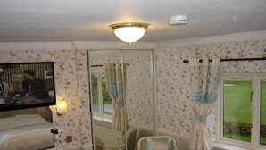 Habitación de hotel con cama, escritorio, silla, televisión y un espejo grande.