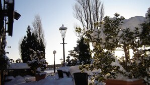 Un espacio al aire libre cubierto de nieve, con una farola, bancos y árboles cargados de nieve.
