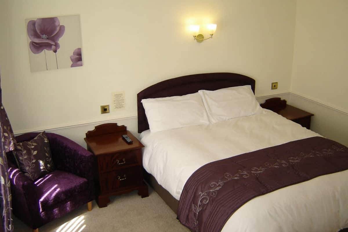 A neatly arranged bedroom with a large bed, a nightstand, a chair, and a wall-mounted light fixture.
