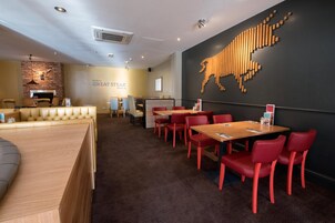 A restaurant interior with a bar area, red chairs, and a wall-mounted wooden design.