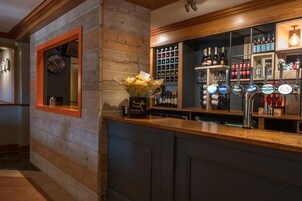 Zona de bar con un reloj, estantes llenos de botellas y grifos de cerveza.