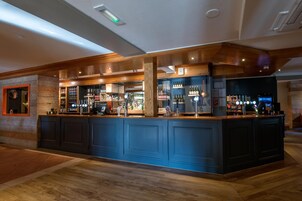 A bar area with wooden paneling, a counter with bottles, and a clock on the wall.