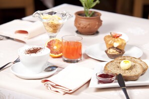 Mesa de café da manhã com xícara de café, copo de suco de laranja, muffin, fatia de pão com manteiga e um potinho de geleia.