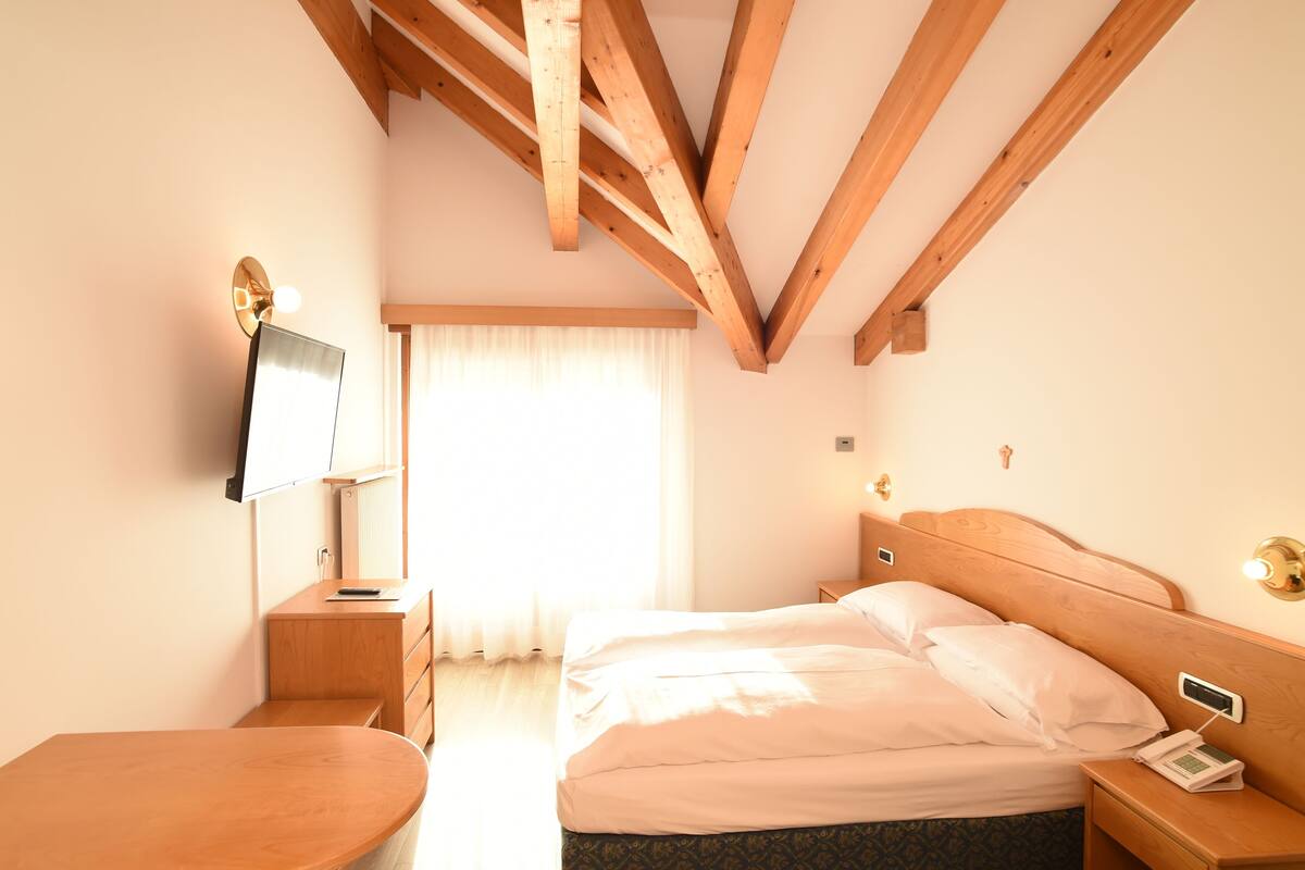Une chambre d’hôtel avec un plafond en bois, un lit, une table de chevet, une télévision et une fenêtre avec des rideaux.