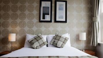 A neatly made bed with plaid bedding, two framed artworks on the wall, and a lamp on either side.