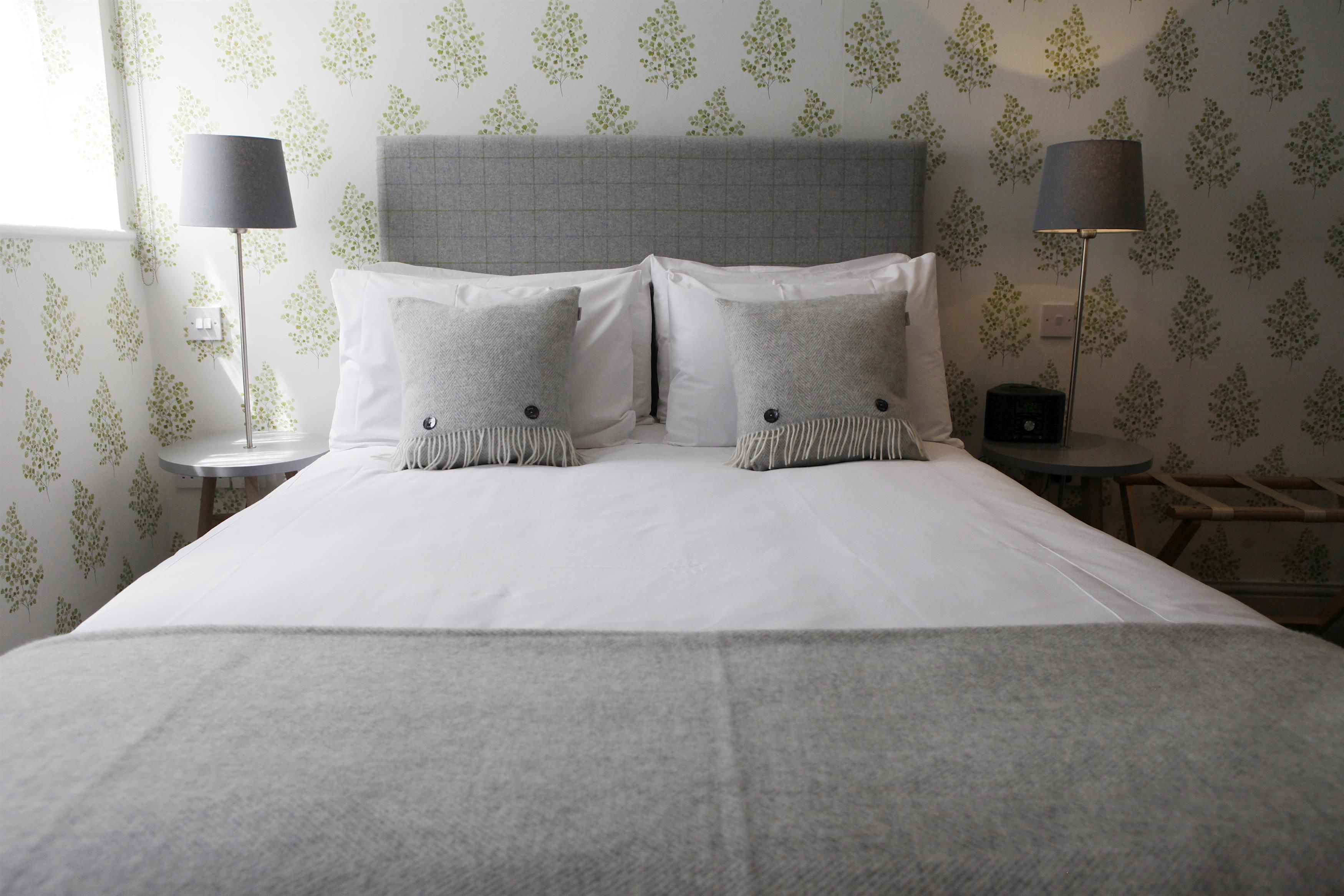 A neatly made bed with a grey headboard, two bedside lamps, and a patterned wallpaper.