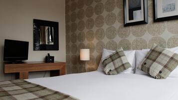 Habitación de hotel con cama, televisor sobre un soporte de madera, lámpara y pared con diseño.