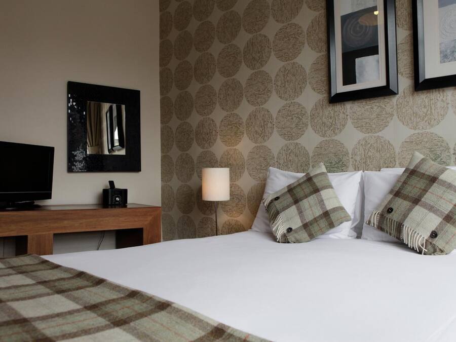 Habitación de hotel con cama, televisor sobre un soporte de madera, lámpara y pared con diseño.