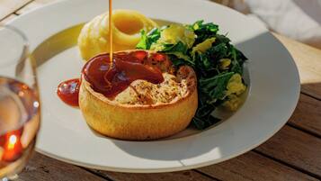 A meal with a baked item topped with sauce, a side of greens, and fries on a white plate.