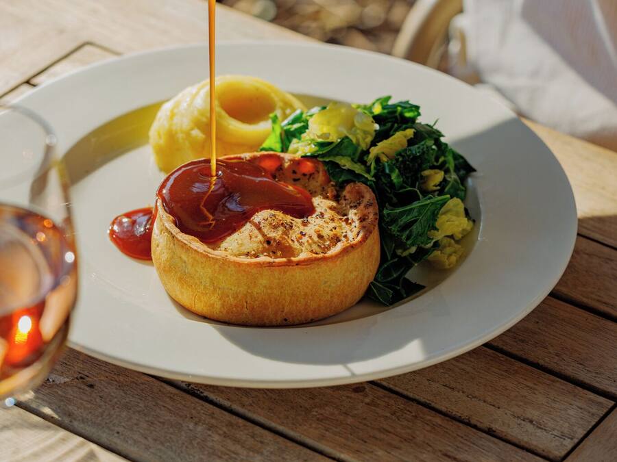 A meal with a baked item topped with sauce, a side of greens, and fries on a white plate.