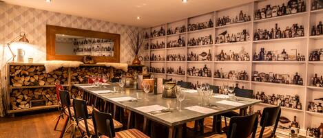 Comedor con una mesa larga dispuesta para seis comensales, rodeada de sillas con cojines a rayas. Se ve un espejo y una estantería con numerosas botellas al fondo.