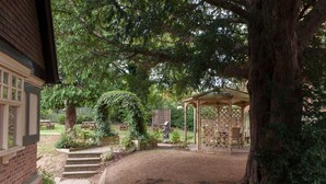 A covered outdoor seating area with a wooden gazebo, surrounded by trees and a brick building. - Heart of England, Northampton by Marston's Inns (Northampton)