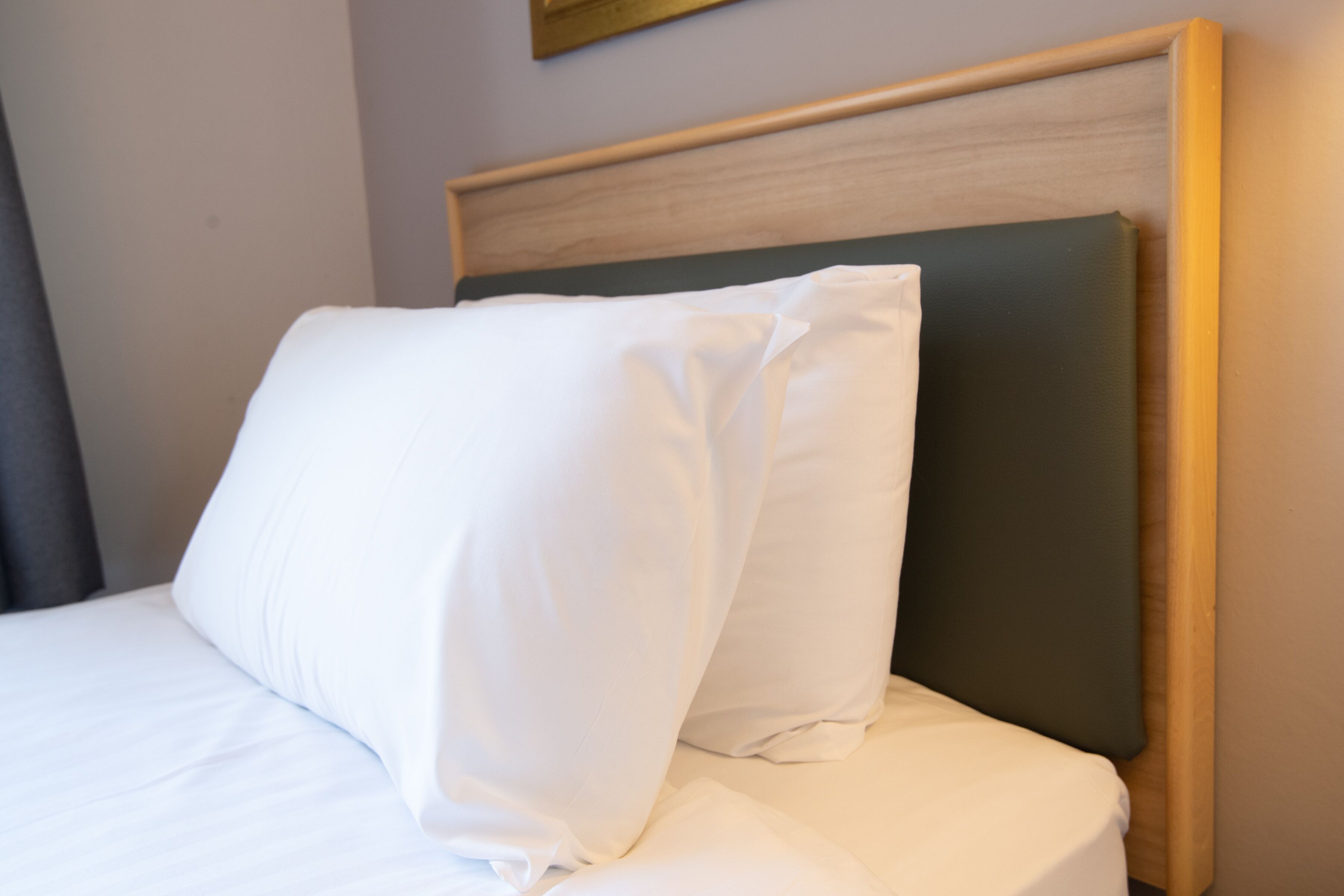 A neatly made bed with white bedding and a wooden headboard.
