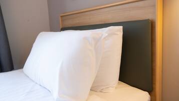 A neatly made bed with white bedding and a wooden headboard.