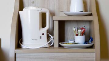 A kitchenette with a white electric kettle, a white cup, and a cup holder with condiments.