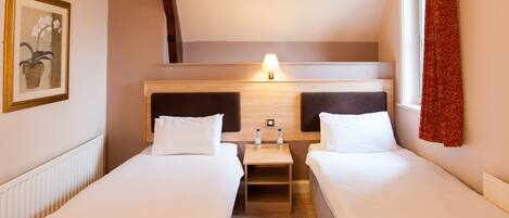 A hotel room with two beds, a nightstand with a lamp, and a framed picture on the wall.