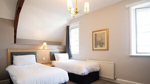 A hotel room with two beds, a chandelier, a radiator, and a window with curtains. - Heart of England, Northampton by Marston's Inns (Northampton)