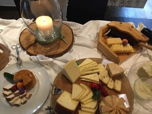Un plateau de fromages comprenant différents types de fromages et des accompagnements, une bougie dans un porte-bougie en verre et un ensemble d’ustensiles en bois pour découper le fromage.