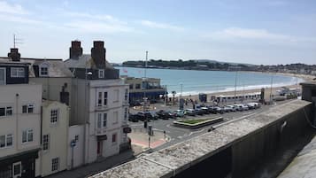A coastal town with a promenade overlooking the beach, a parking area, and buildings with commercial establishments.