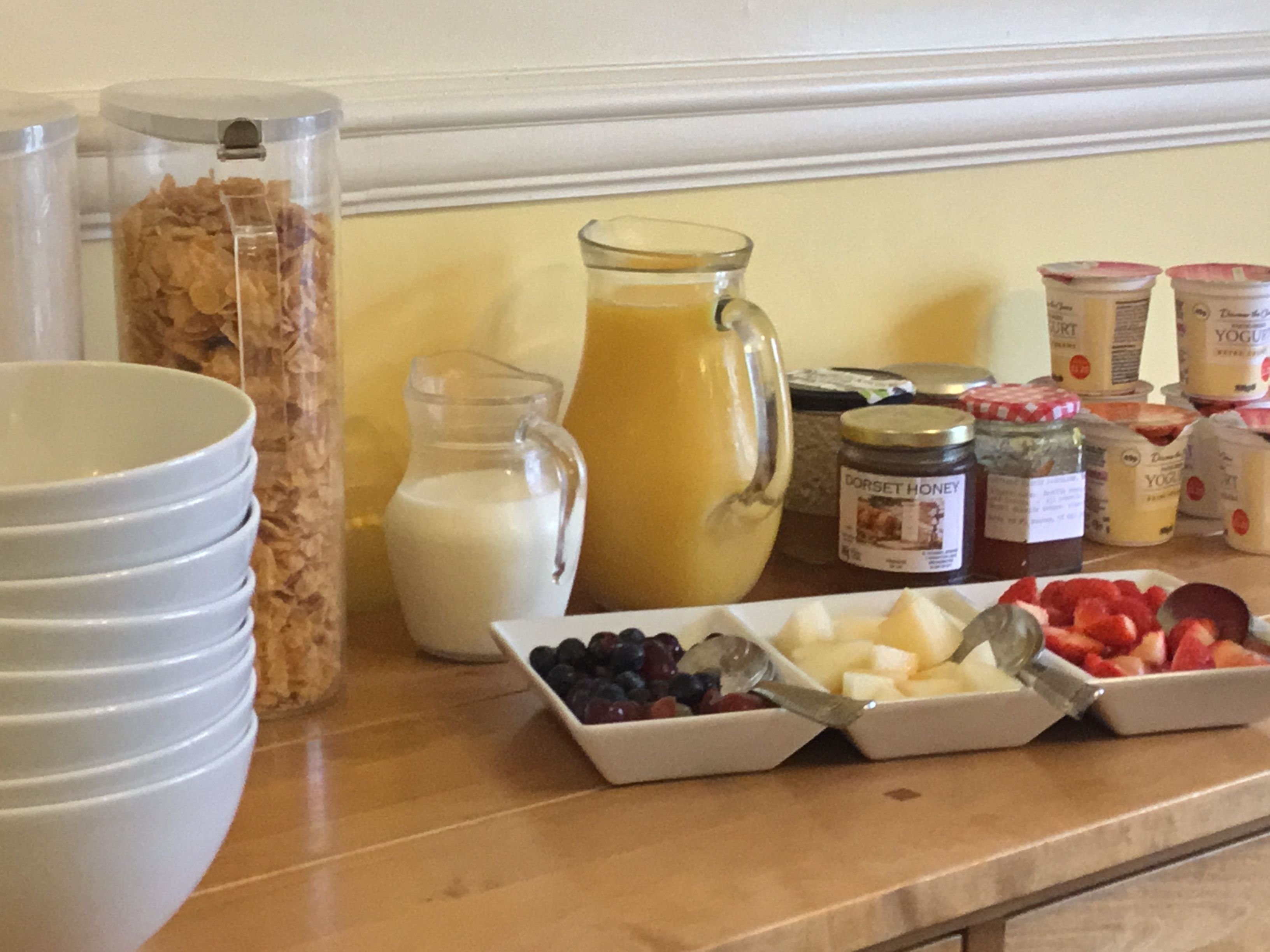 A breakfast buffet with cereal, milk, juice, yogurt, and fresh fruits.