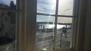 Blick aus einem Fenster auf eine belebte Straße mit Fahrzeugen und einem Gewässer im Hintergrund.