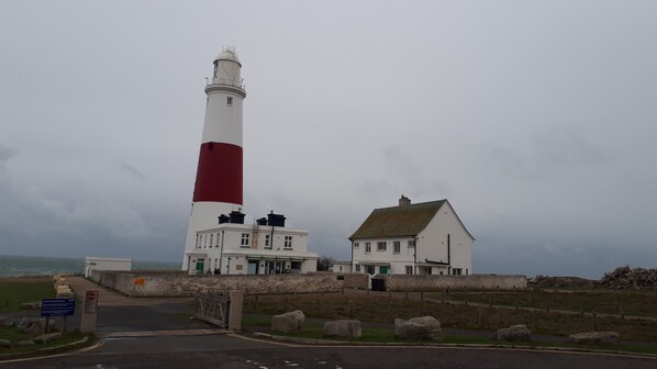 A lighthouse with a red and white tower, a white building with a green roof, and a stone wall.