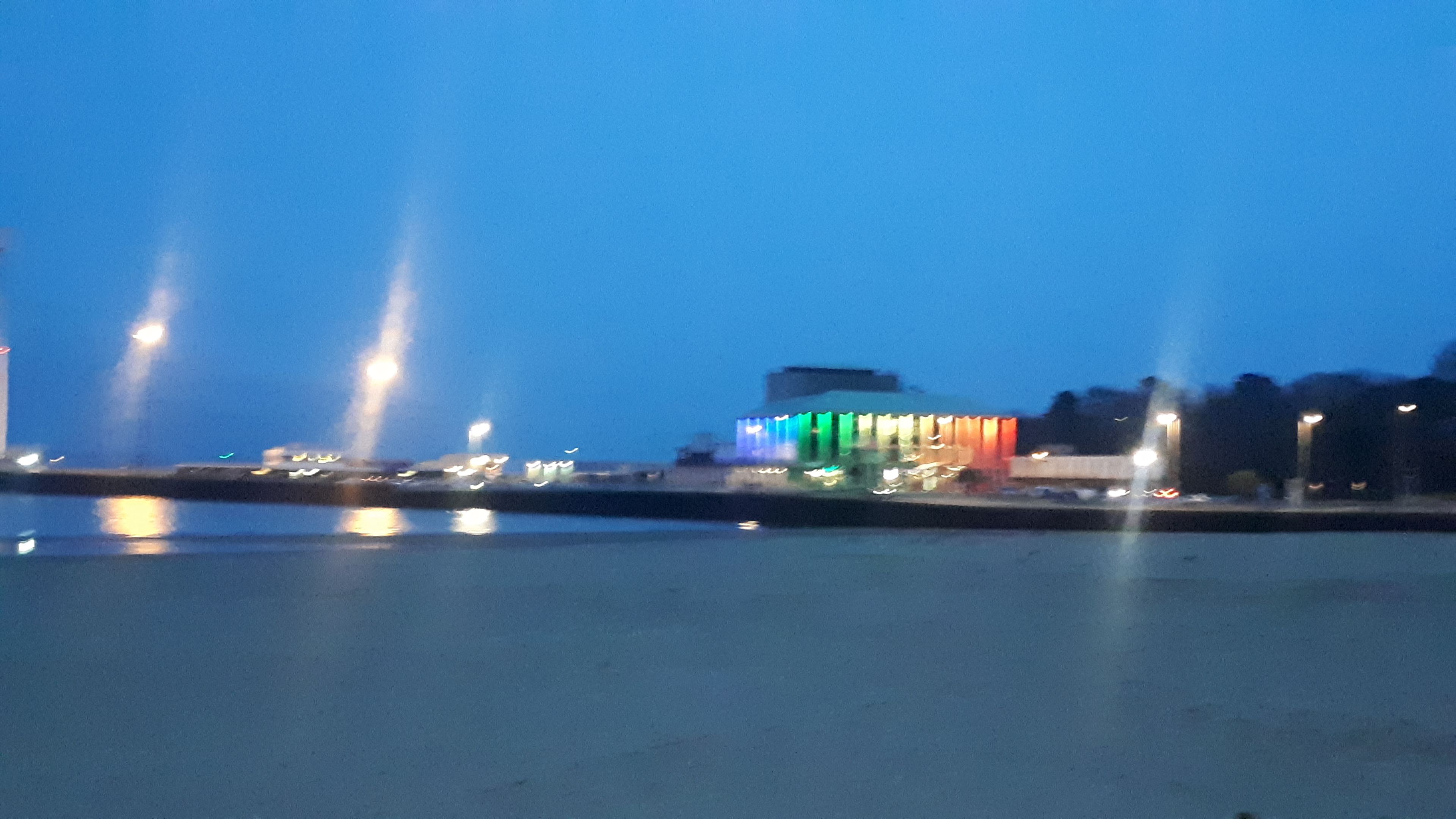 A waterfront view with a building illuminated by colorful lights.