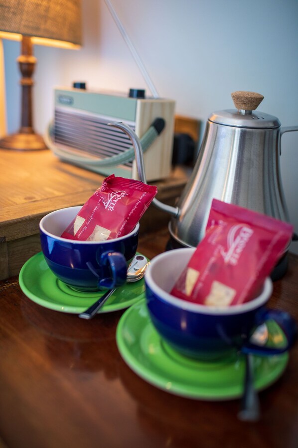 Two cups with coffee packets on a wooden table, a coffee pot, and a vintage radio in the background.