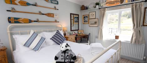 Un dormitorio ordenado con cama, almohadas, una mesita de noche, lámpara y ventana con cortinas.