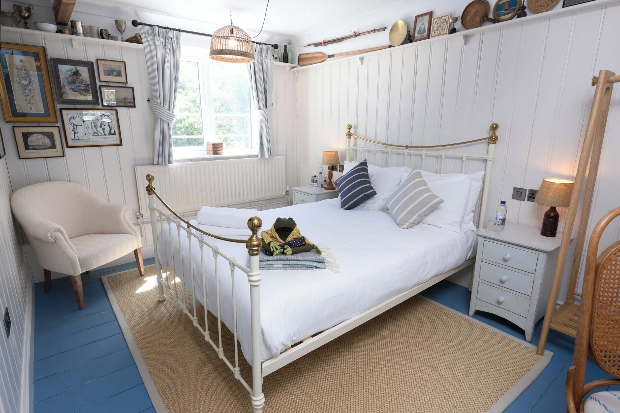 Ein Schlafzimmer mit einem weißen Himmelbett, einem Sessel, einem Nachttisch und einem Fenster mit Vorhängen.