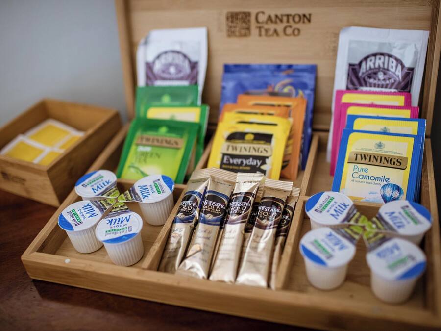 A wooden tray with various tea and coffee products, including Twinings and Arriba brands, and Nescafe Gold packets.