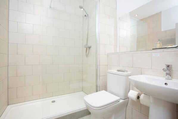 A modern bathroom with a glass shower enclosure, a white toilet, and a sink with a mirror above it. - Hotel Continental (Whitstable)