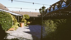A courtyard with a tiled roof, potted plants, and string lights. - The New Chichester Hotel (Wickford)