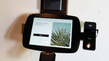 A digital check-in kiosk with a screen displaying a welcome message for The New Chichester Hotel, options for check-in, room keys, and check-out.