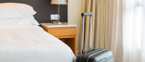 A hotel room with a bed, a nightstand, a lamp, and a suitcase.