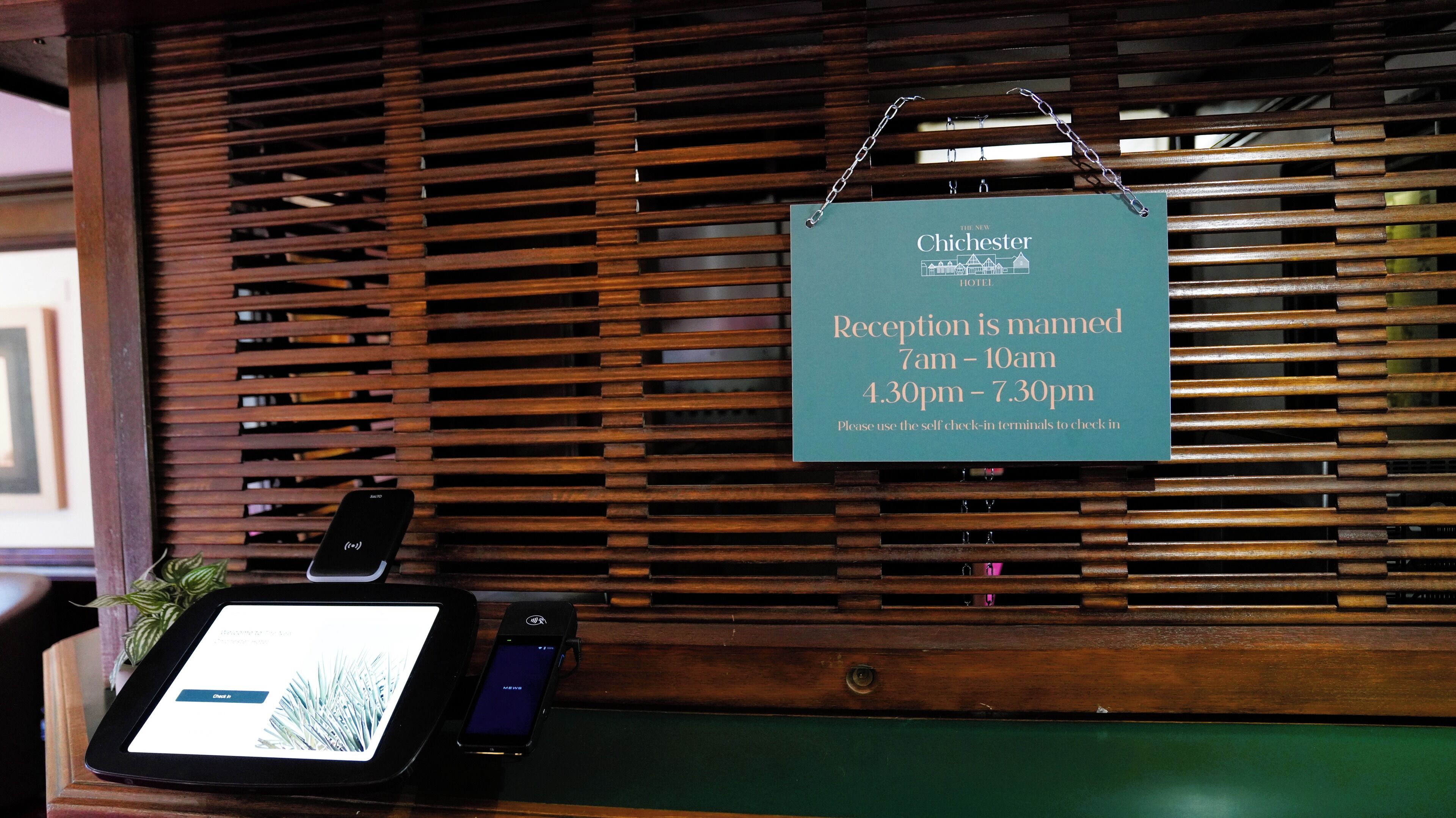 A reception desk with a sign indicating reception hours and a self-check-in terminal.