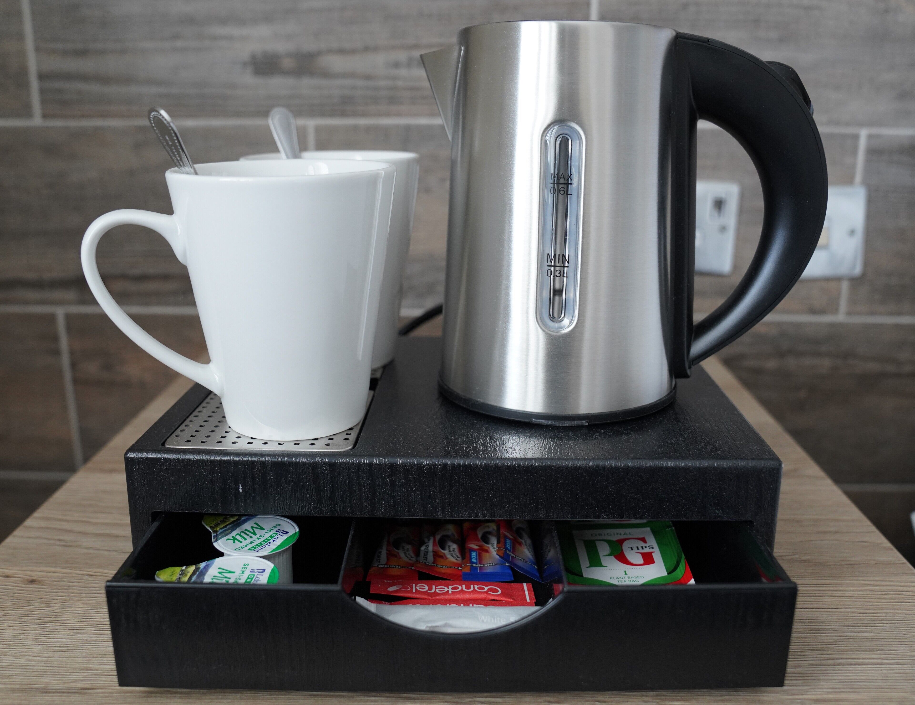 A stainless steel kettle and a white mug on a tray, with tea bags and a box of PG Tips tea bags underneath.