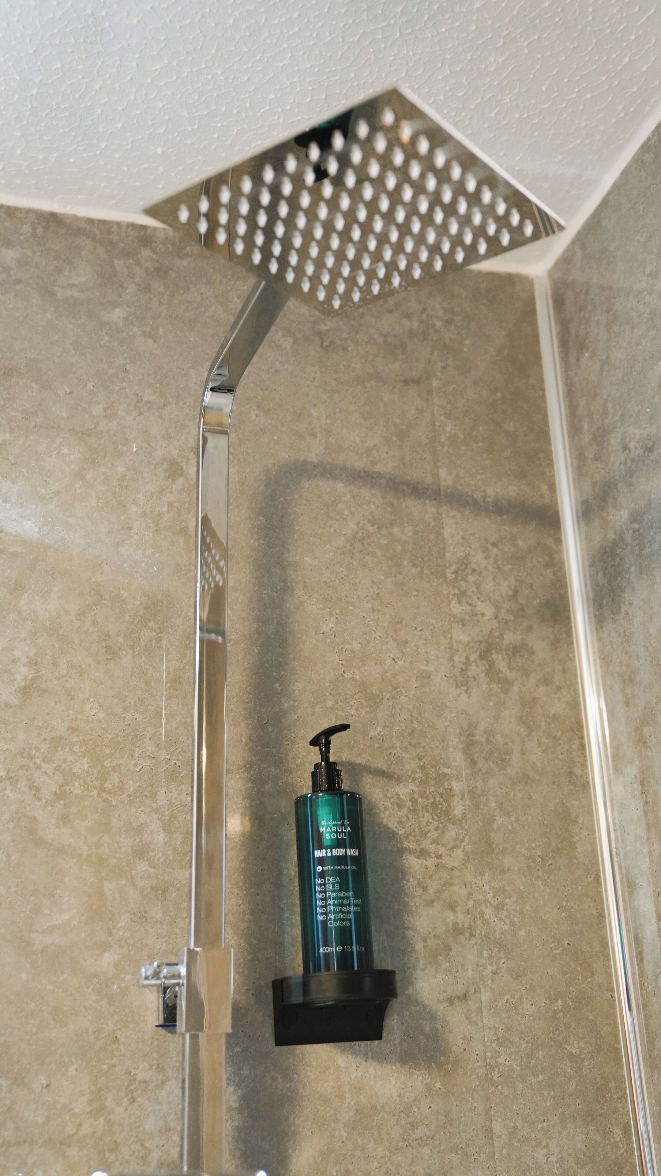 Ducha con cabezal de lluvia y una botella de jabón para cabello y cuerpo en un estante.