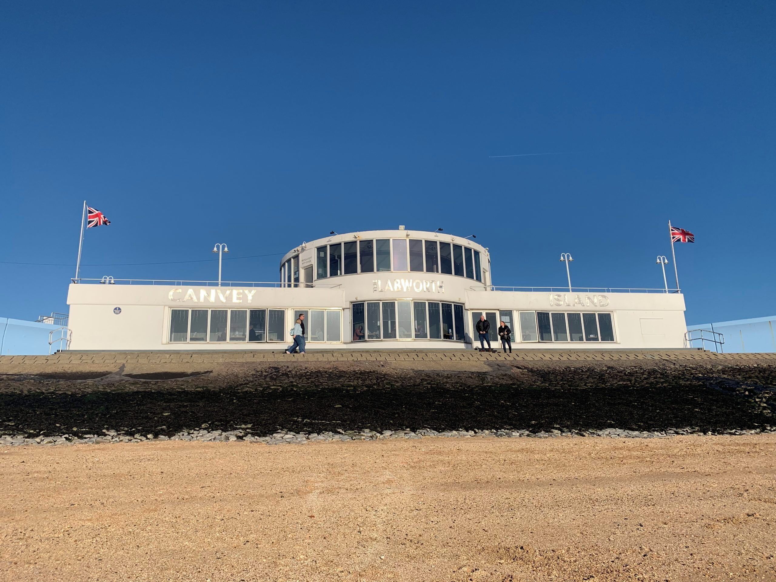 Un edificio con las palabras "CANVEY" e "ISLAND" en su fachada, que presenta una sección central circular y dos mástiles con banderas.