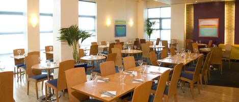 A restaurant with multiple tables and chairs, large windows, and wall art.