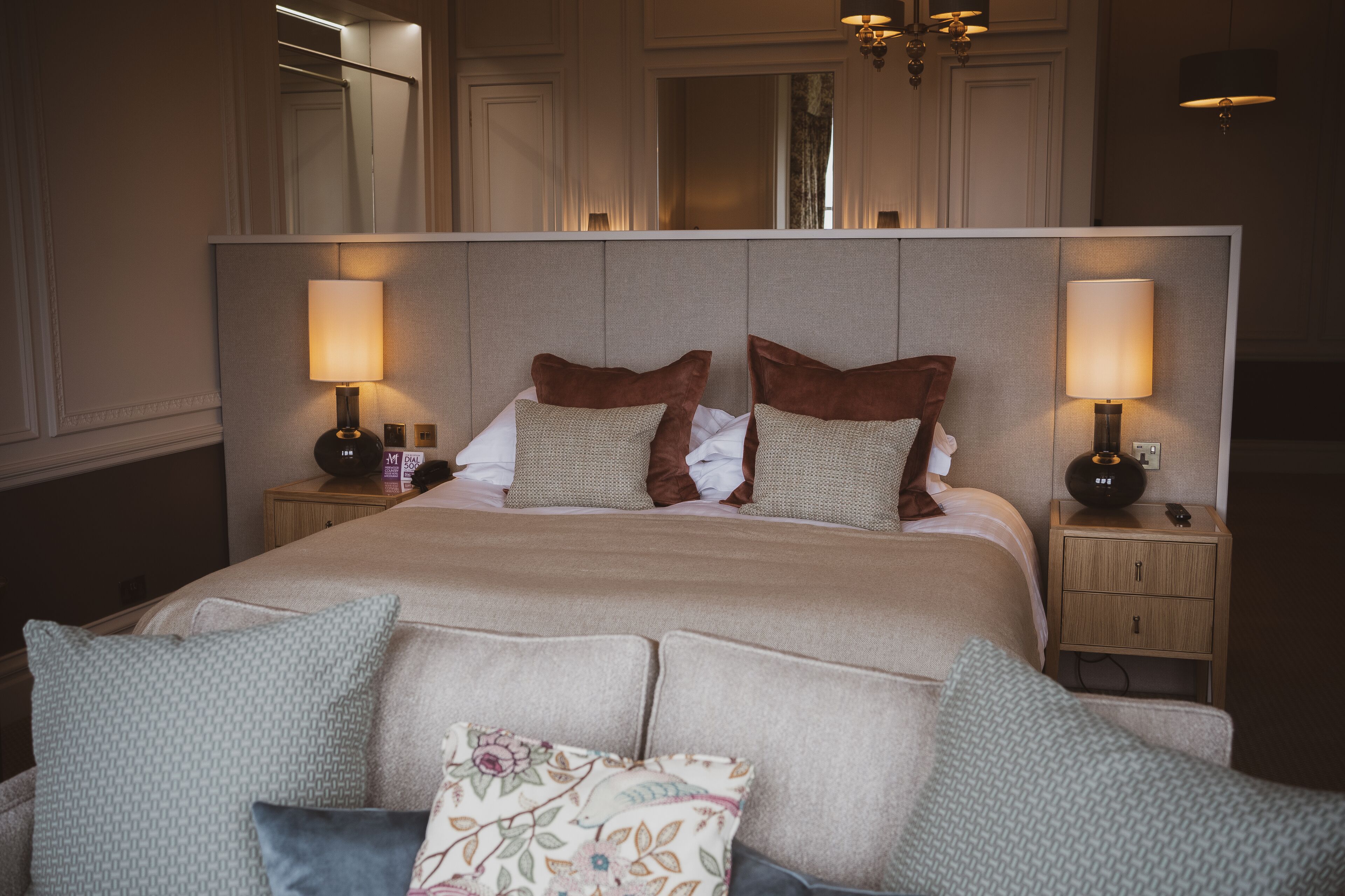 A neatly made bed with a headboard, two bedside tables with lamps, and a floral pillow.