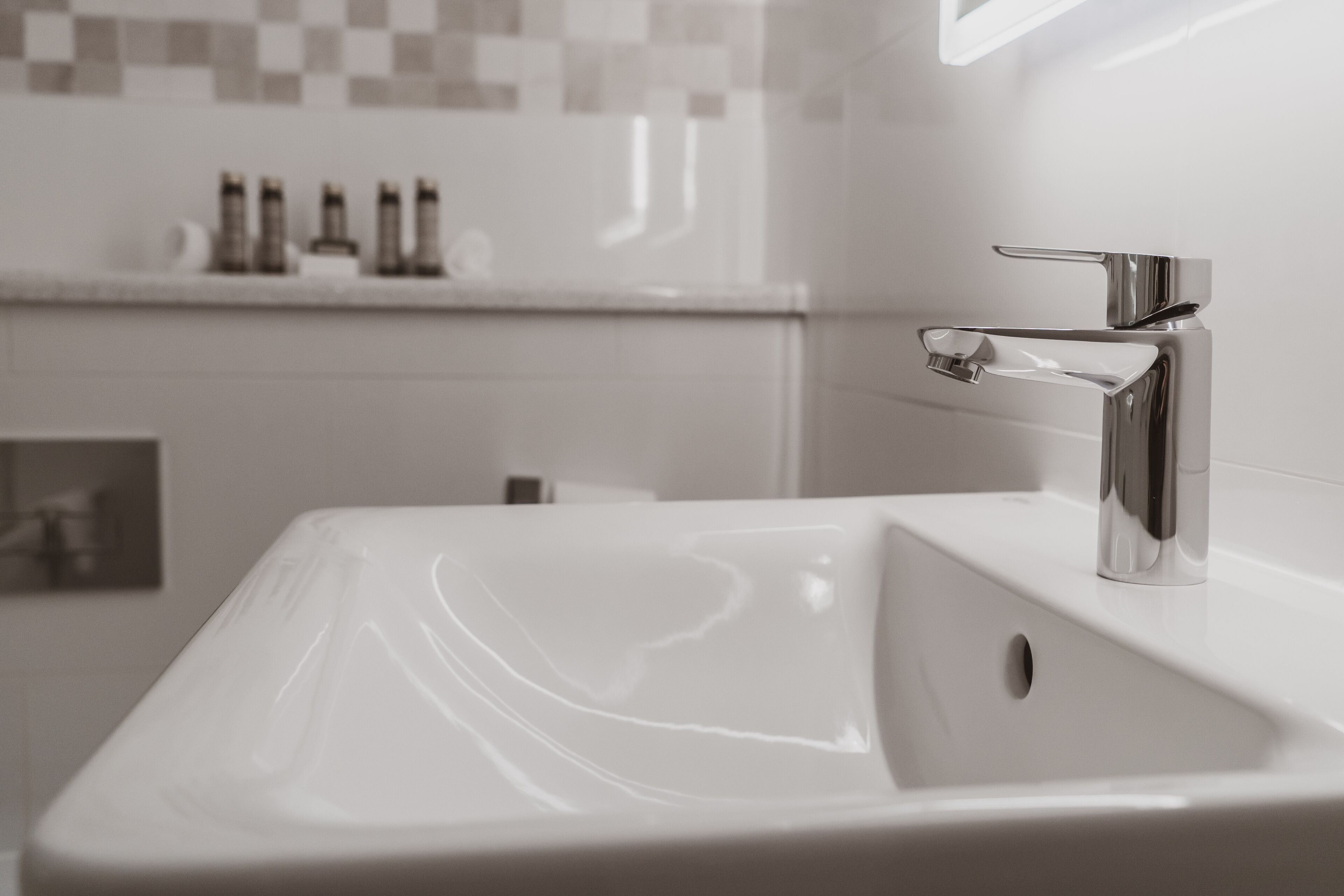 A modern bathroom with a white sink, chrome faucet, and a tiled backsplash.