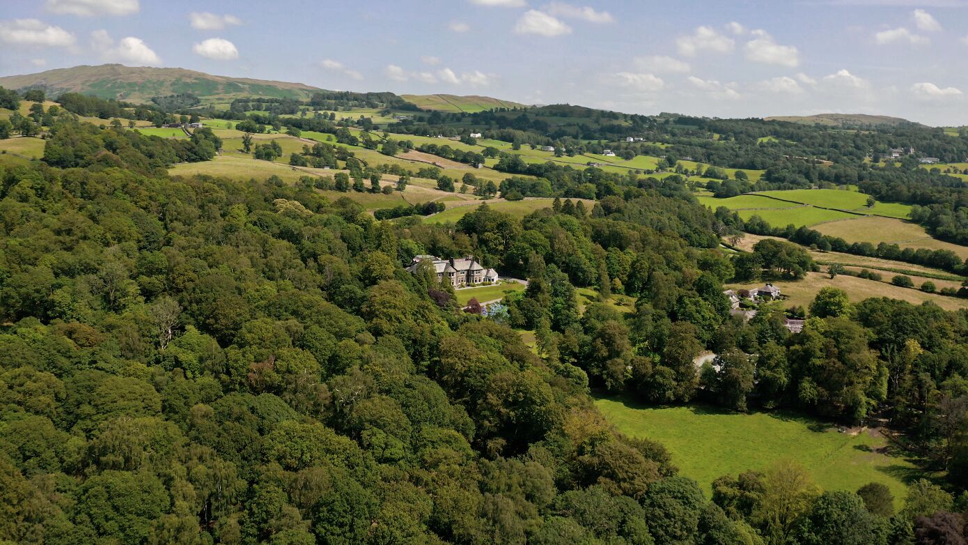 A rural landscape with rolling hills, scattered houses, and dense forests.