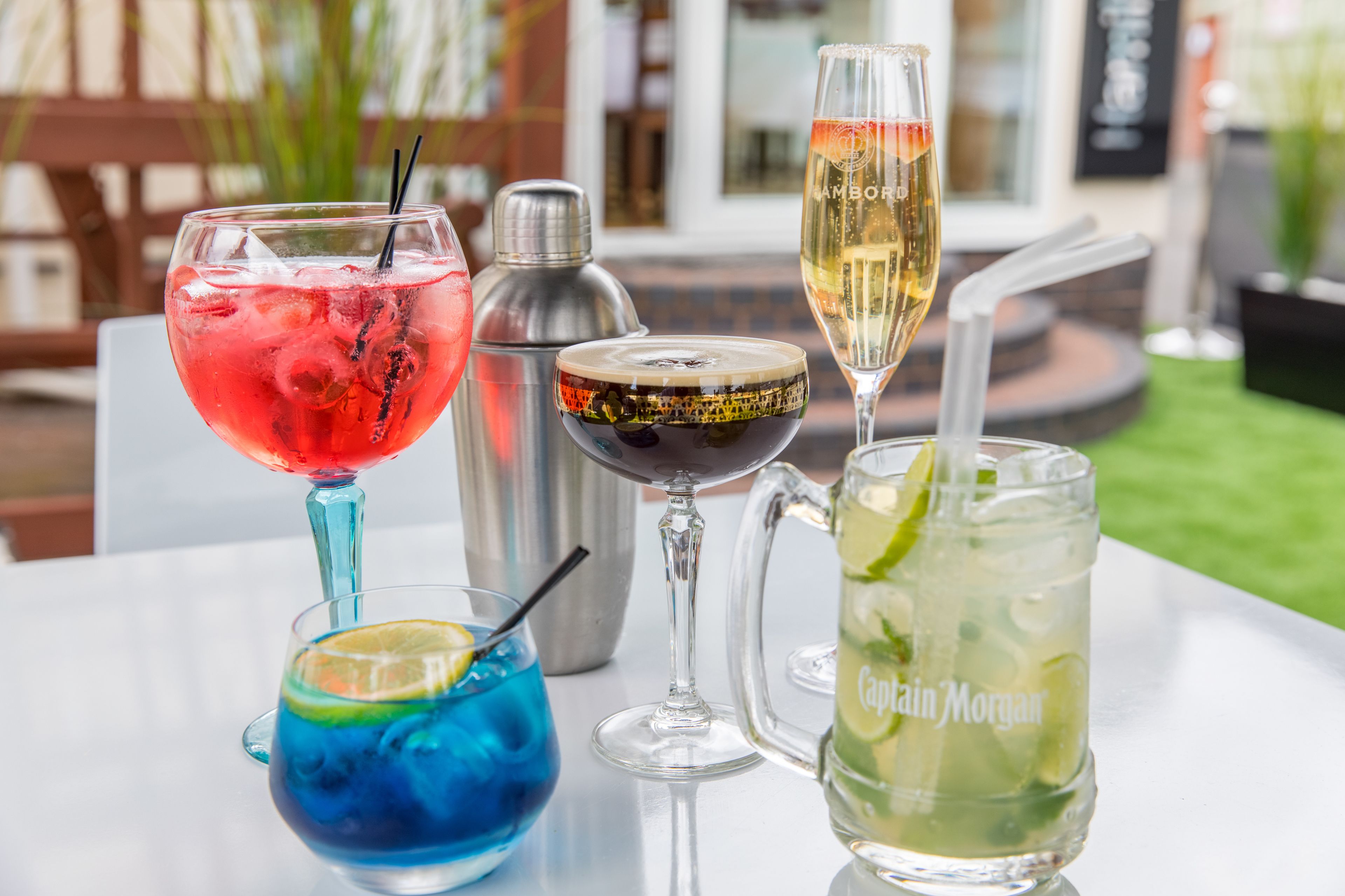 A table with various drinks including a red cocktail, a blue cocktail, a champagne flute, and a pitcher labeled "Captain Morgan".