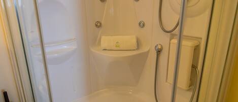 A glass-enclosed shower stall with a white bathtub, a towel rack, and a soap dispenser.
