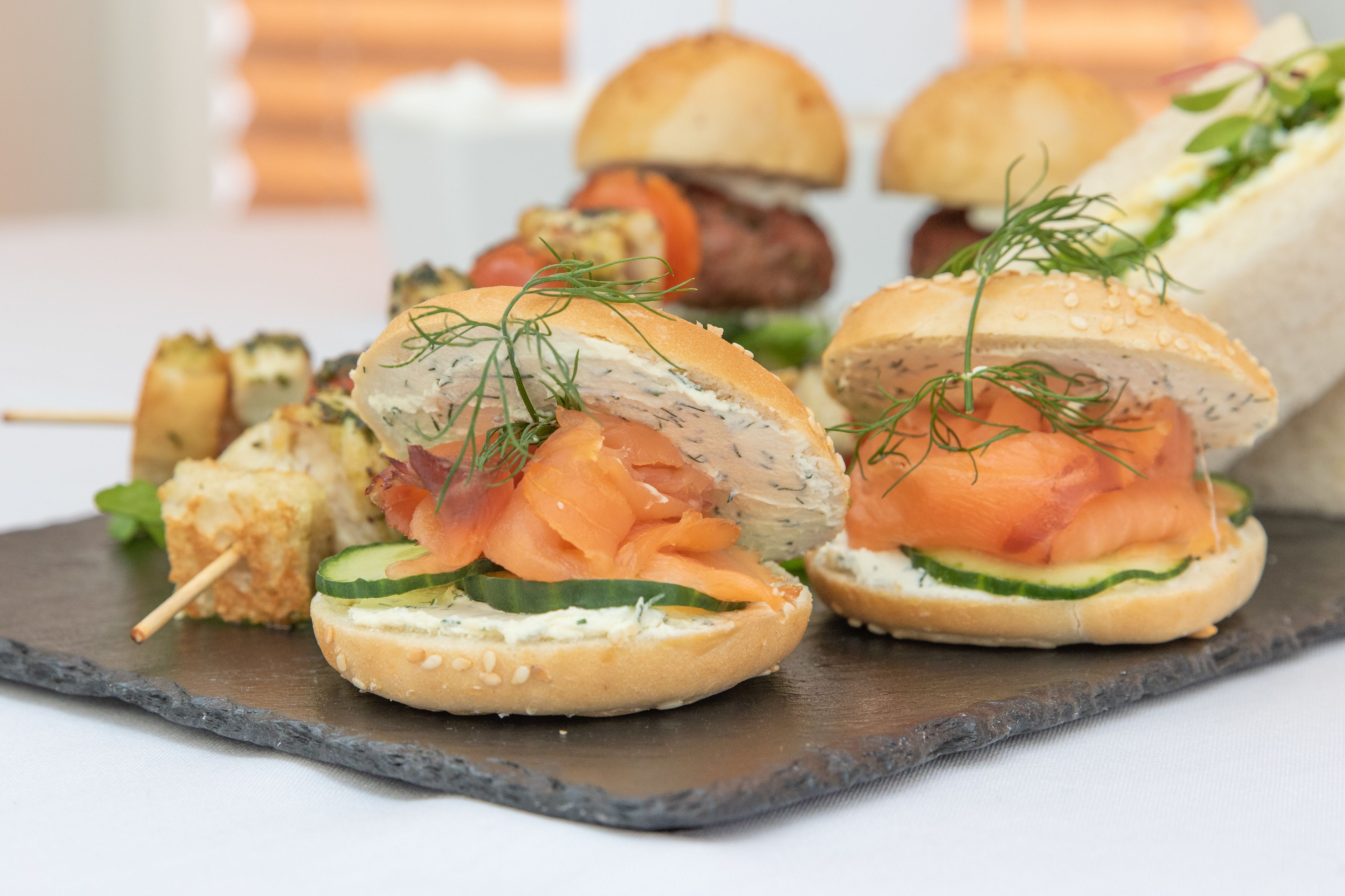 A variety of appetizers including smoked salmon on a bun, a sandwich, and skewers, all served on a slate board.