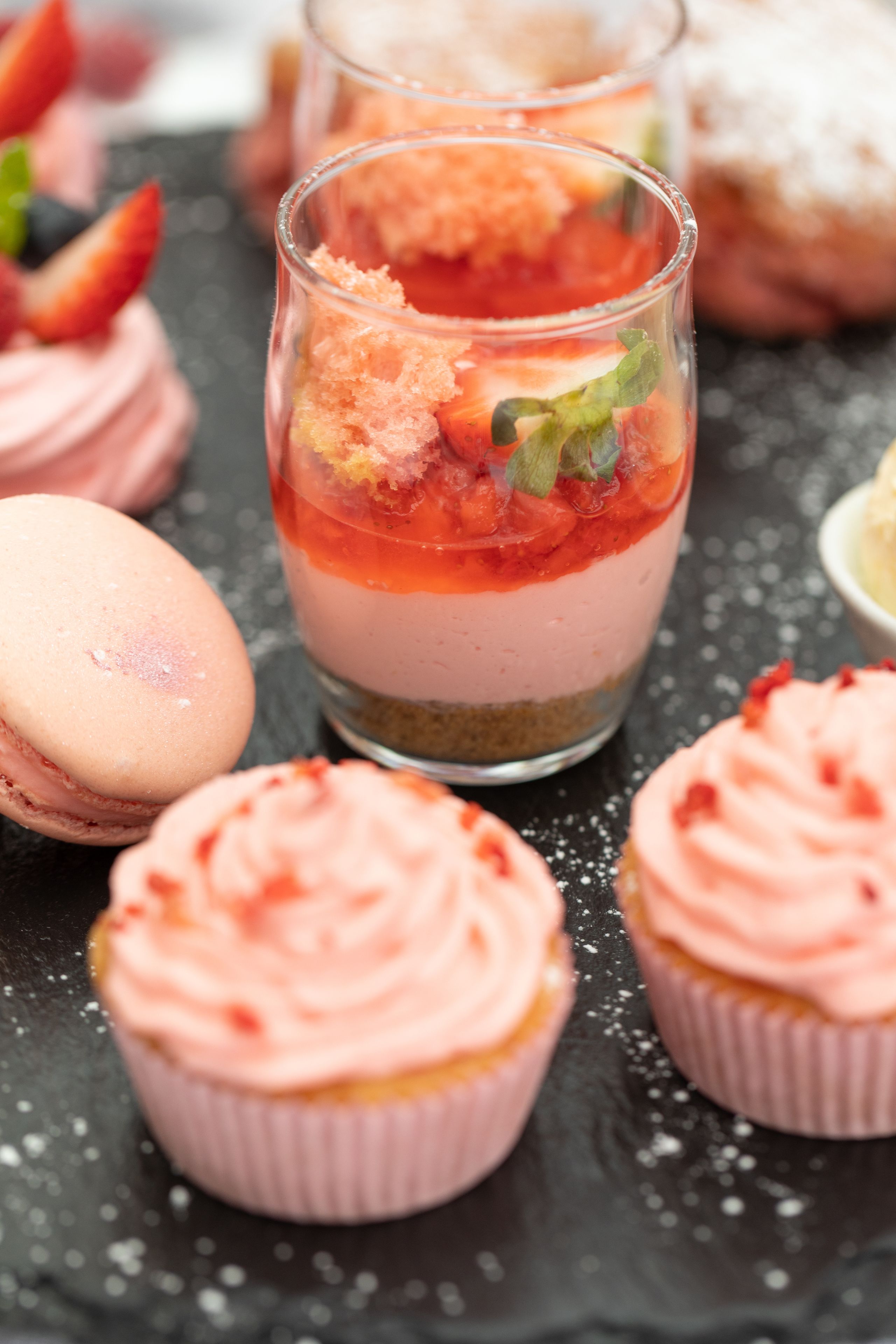 Eine Dessertplatte mit gestaffelten Desserts in Rosa und Rot, Macarons und Cupcakes.